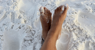 Two brown adult feet crossed over each other in the white sand