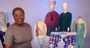 Photo of Emmy award-winning journalist Joyce Brewer in a TV studio surrounded by Frozen merchandise like Anna and Elsa dresses to celebrate the film's 10th anniversary